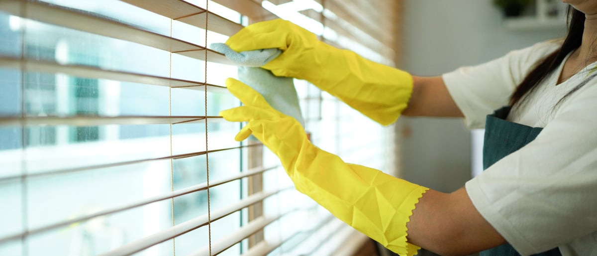 Gloved hand dusting wooden Venetian blinds